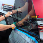 Technician applies window film to side of vehicle in an automotive workshop.