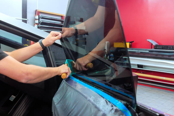 Technician applies window film to side of vehicle in an automotive workshop.