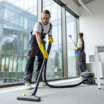 Vacuum cleaning. Young man in uniform vacuum cleaning the floor in the conference room